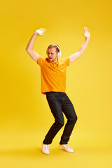 Fototapeta na wymiar Full-length portrait of young man wearing style casual outfit and dancing listening music in headphones isolated yellow studio background.