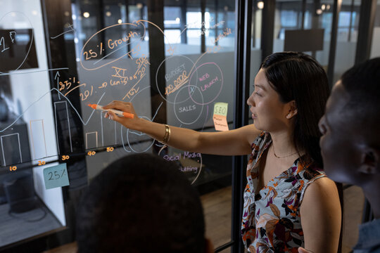 Happy diverse male and female colleagues brainstorming at glass wall in office