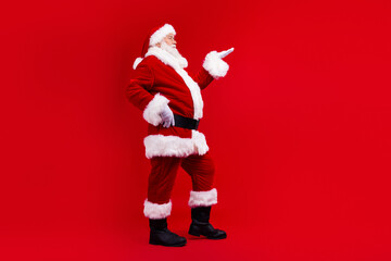 Side profile full body photo of pleasant santa claus with white beard arm demonstrate sale empty space isolated on red color background