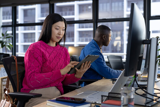 Focused asian casual businesswoman using tablet at desk with diverse colleague in office