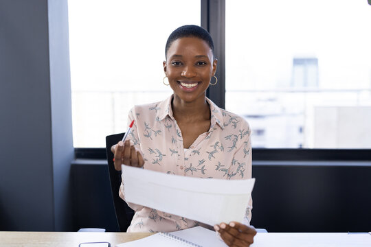 Happy african american casual businesswoman having video call, sitting at desk holding document