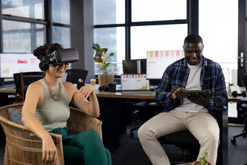 Happy diverse male and female colleague in casual office meeting using vr headset and tablet