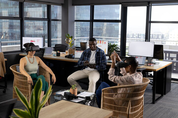 Happy diverse male and female colleagues in casual office meeting using vr headsets and tablet