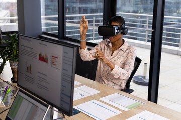 African american casual businesswoman wearing vr headset using virtual interface at desk in office