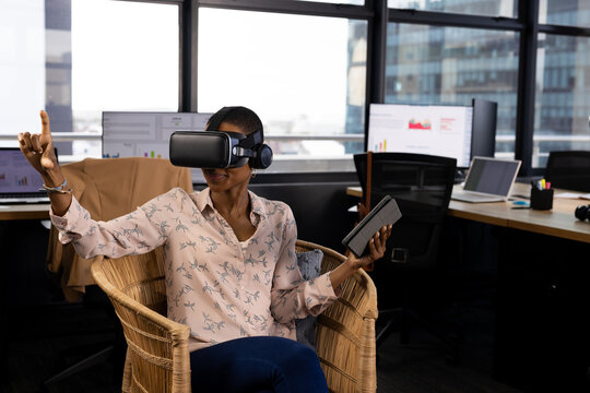 African american casual businesswoman in vr headset using tablet and virtual interface in office