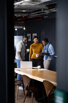 Happy diverse male and female colleagues using tablet and laptop standing in office, copy space