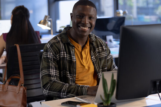 Portrait of happy african american casual businessman sitting at desk using laptop in office