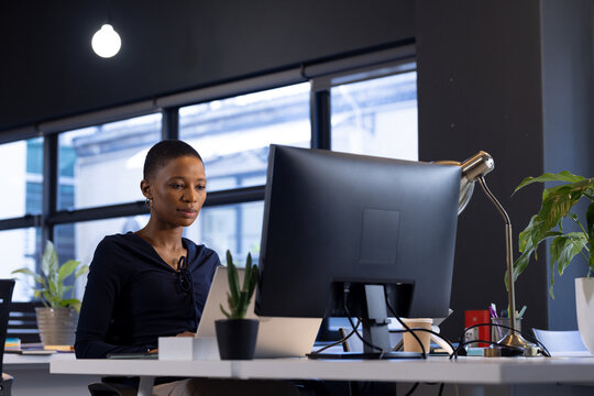 Focused african american casual businesswoman sitting at desk using laptop in office, copy space