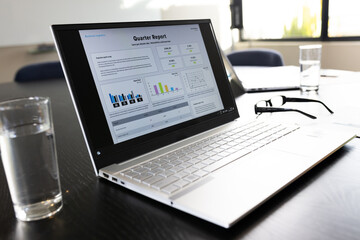 Laptop with quarter report text and graphs on screen on table in office meeting room