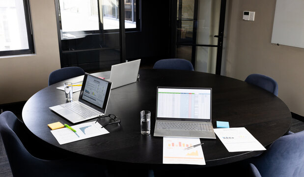 Paperwork and laptops with reports and data on screens on table in office meeting room, copy space
