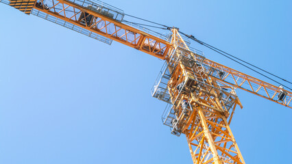 The tower construction crane is orange against the blue sky. Rotary boom of the tower crane. Construction in the city. The cabin of the tower crane. Steel construction of the crane. © Eduard Belkin