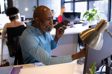 Senior african american casual businessman talking on smartphone sitting at desk in office
