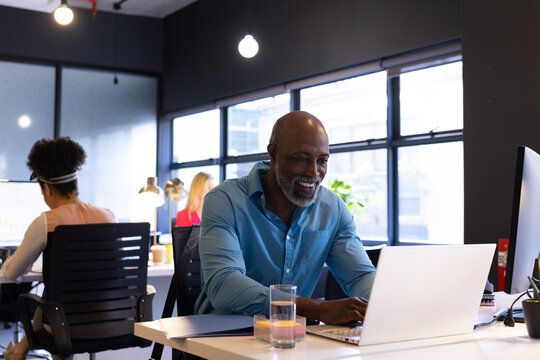 Happy senior african american casual businessman using laptop sitting at desk smiling in office