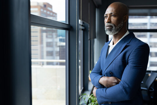 Thoughtful senior african american businessman standing looking out of window in office, copy space