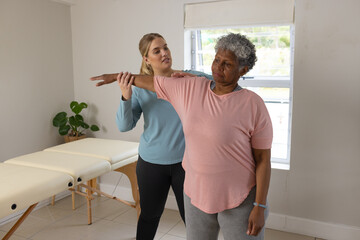 Caucasian female physiotherapist and senior afrcian american female patient stretching, copy space