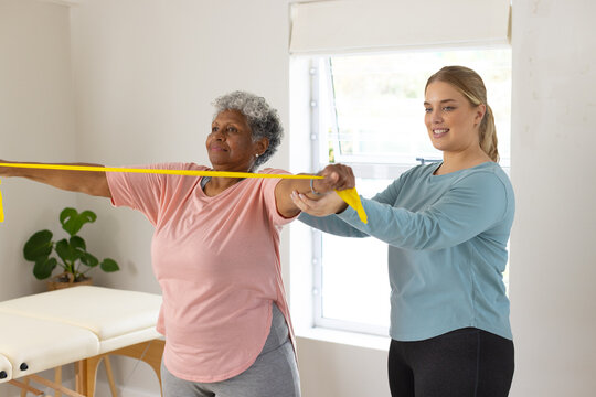 Caucasian female physiotherapist and senior afrcian american female patient with band, copy space