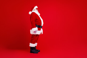 Fototapeta na wymiar Side profile full body photo of optimistic grandfather wear santa costume look at sale empty space isolated on red color background