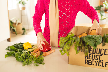 Midsection of biracial woman in hijab unpacking groceries from cardboard box in kitchen