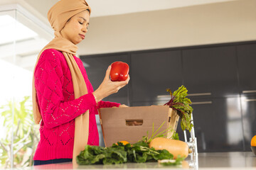 Biracial woman in hijab unpacking groceries from cardboard box in kitchen