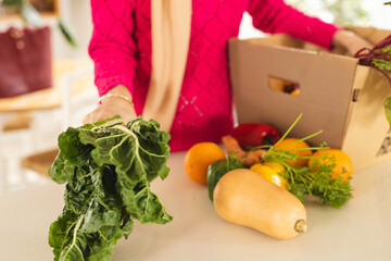 Midsection of biracial woman in hijab unpacking groceries from cardboard box in kitchen
