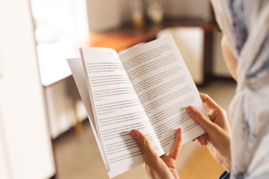 Biracial woman in hijab reading book in living room