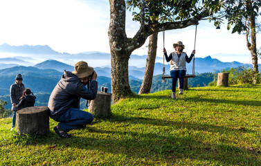 Photographer taking pictures of woman sitting on swing with mountains view background, camping concept