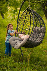 A girl puts things in order on a hanging chair that stands in nature