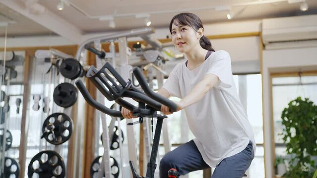 スポーツジムのエアロバイクで運動する女性（健康・ダイエット）