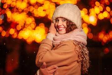 A captivating curly-haired young lady in the evening, framed by the glow of lights and a decorated...