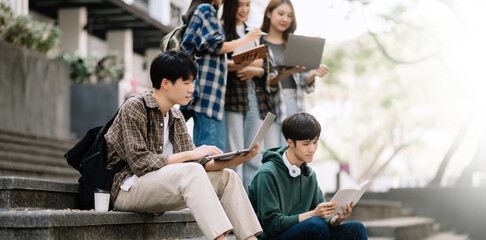 Asian Students are studying the campus park. Young people are spending time together. Reading book, working with laptop, tablet while sitting on stairs