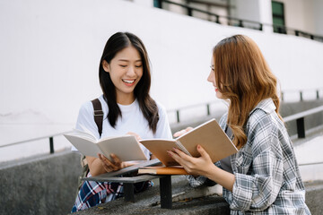 Asian Students are studying the campus park. Young people are spending time together. Reading book, working with laptop, tablet while sitting on stairs