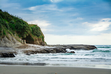 Sunset at Muriwai beach with waves splashing against the rocks and fishermen silhouettes in the...
