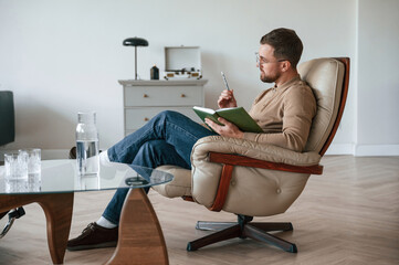 Male psychologist is sitting in the chair with notepad in the office