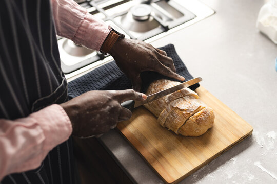 Midsection of mature african american man cutting freshly baked bread in sunny kitchen, copy space