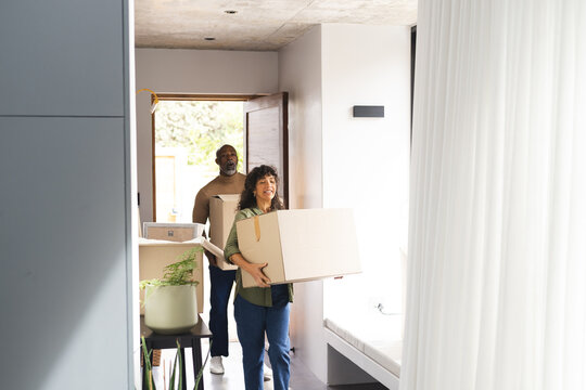 Happy diverse couple carrying packing boxes into new home, copy space