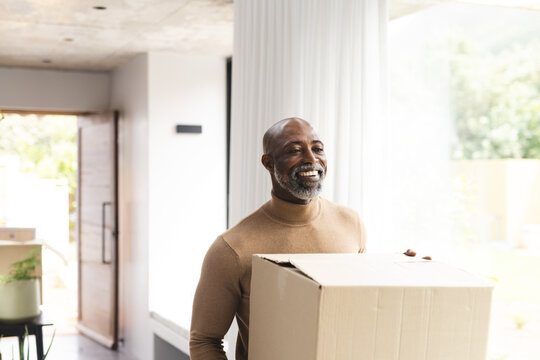 Happy african american mature man carrying packing box into new home, copy space