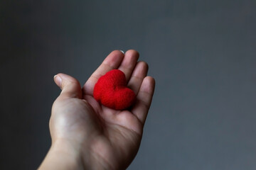 Red heart in woman's hand on grey background. The concept of charity, love, donate and helping hand. International cardiology day. A woman gives a red heart to the man's hands