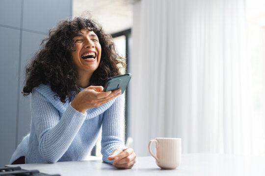Happy mature caucasian woman talking on smartphone laughing in sunny kitchen, copy space