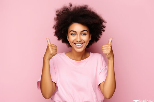 radiant African American woman wearing a pink shirt gives two thumbs up, symbolizing her victorious battle against breast cancer within the context of awareness