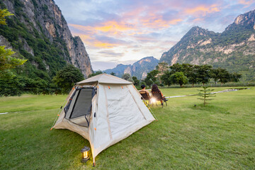 Camping and tent in nature. Adventure lifestyle of man and woman sitting in camp chairs looking at Beautiful sunset over the mountain range and enjoying view of nature. - obrazy, fototapety, plakaty