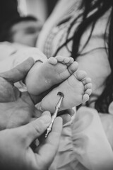 Baptism ceremony of baby. Closeup of tiny baby feet, the sacrament of baptism. Godmother holds child in his arms. Priest stretches hands to child legs. Temple, Orthodoxy. Black and white photo.