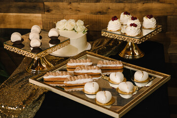Delicious reception luxury ceremony. Candy bar on wedding banquet, birthday party, baptism closeup. Pastries with cream on a golden plate. Table with sweets, candies, and dessert. Side view.