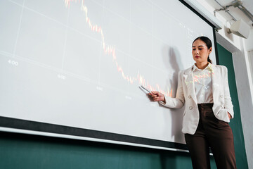A cheerful and confident Asian businesswoman stands, presenting technical graph, bar charts data...