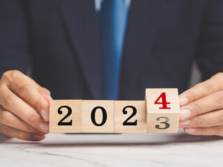 Businessman holds wooden cubes with the numbers 2023 and 2024 for starting a new business plan