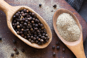 Heap of black pepper, peppercorns in spoon with milled powder on rustic background, dried spice...