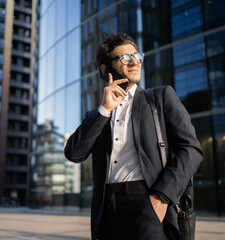 A businessman with glasses in a suit uses a phone. A successful confident man is talking on the phone with a colleague at a startup and a new project at work.