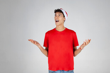 Chico con Gorro de Papá Noel y Camiseta Roja sobre fondo blanco sorprendido por la llegada de la Navidad - obrazy, fototapety, plakaty