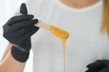 Female cosmetologist holding stick with wax for depilation or sugaring