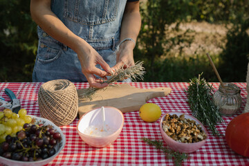 Woman tying fresh rosemary and immortelle with twine. Women's hands and fresh herbs


