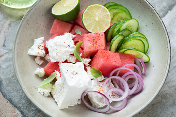 Salad with fresh watermelon, feta cheese, cucumber and red onion served in a beige plate, middle close-up